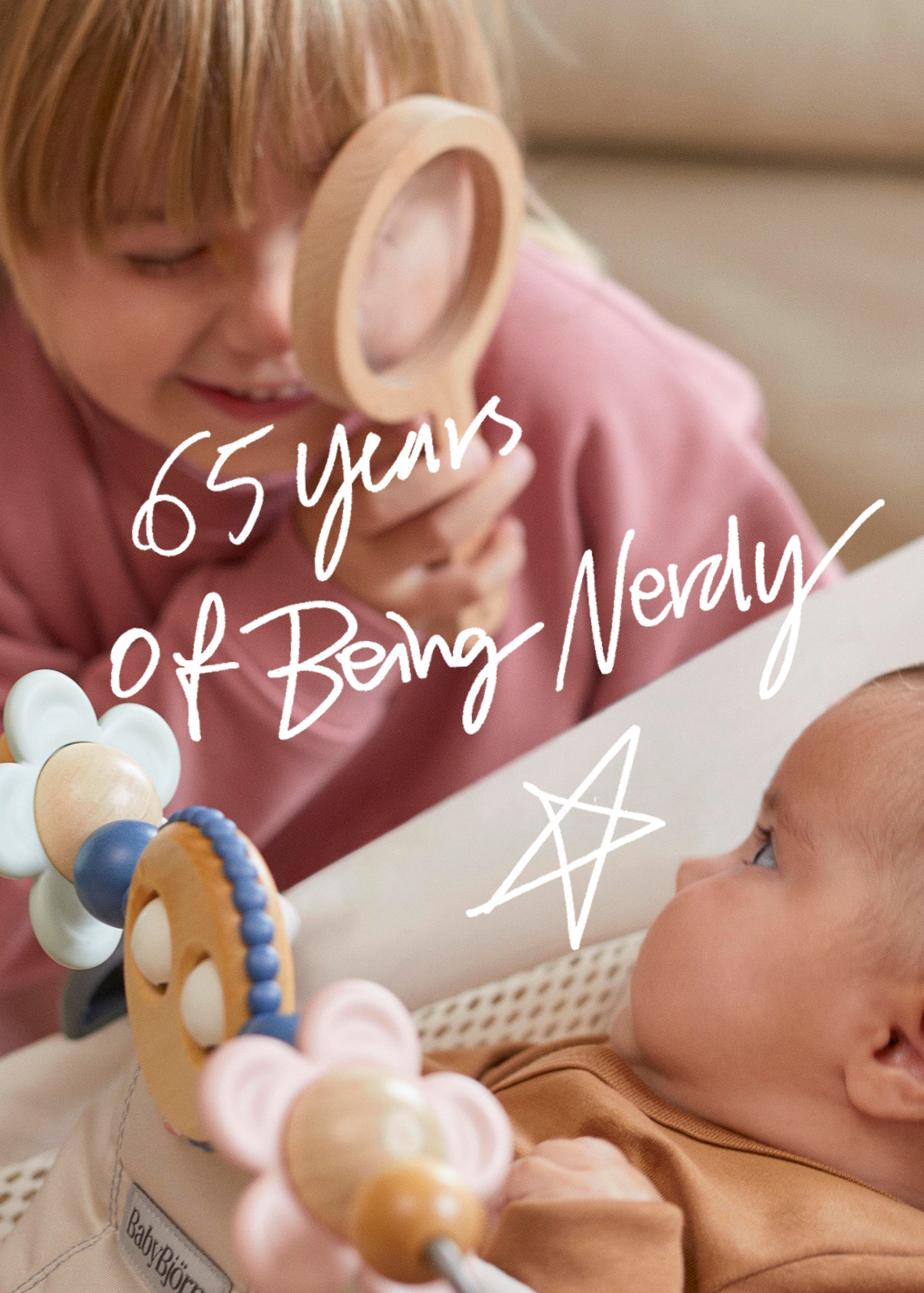 ילד מחייך מבעד לזכוכית מגדלת מעץ לעבר תינוק בעריסה; הטקסט: “65 שנים של להיות בקפדנות” עם כוכב מצויר.