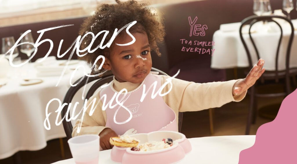 פעוטה יושבת לאכול עם כלי האוכל של בייבי ביורן. כיתוב על גבי התמונה: 65 שנים של לומר לא.