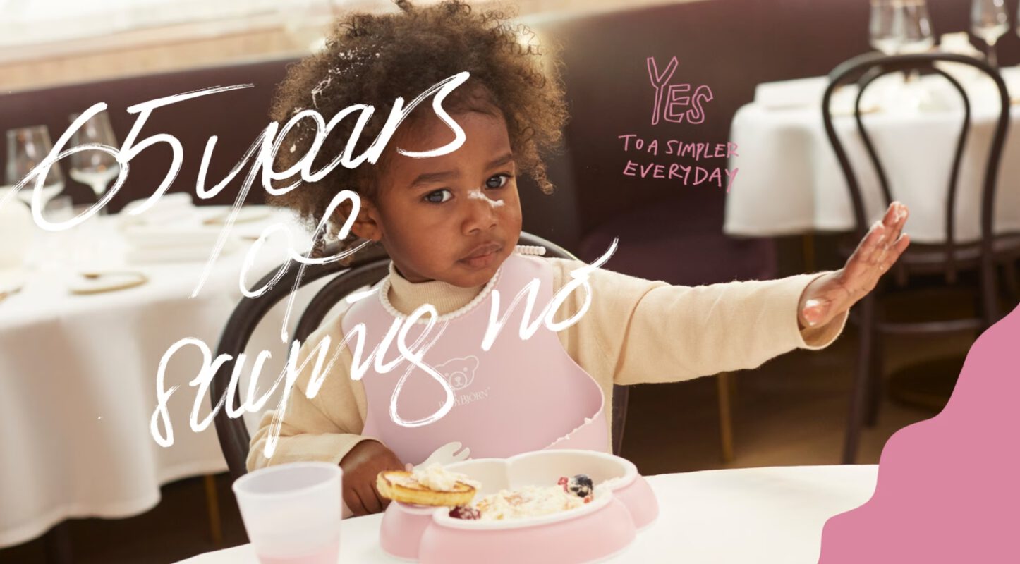 פעוטה יושבת לאכול עם כלי האוכל של בייבי ביורן. כיתוב על גבי התמונה: 65 שנים של לומר לא.